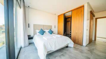 Ein modernes Schlafzimmer mit einem großen Bett, einem begehbaren Kleiderschrank und Blick durch ein großes Fenster.