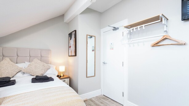 A hotel room with a bed, a bedside table with a lamp, a mirror, a wardrobe, and a coat rack with hangers. - The Wire B4 by Guestz (Warrington)