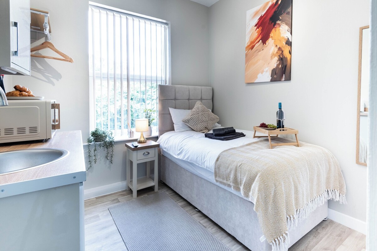 A modern bedroom with a bed, bedside table, lamp, and a view of the outdoors through the window.