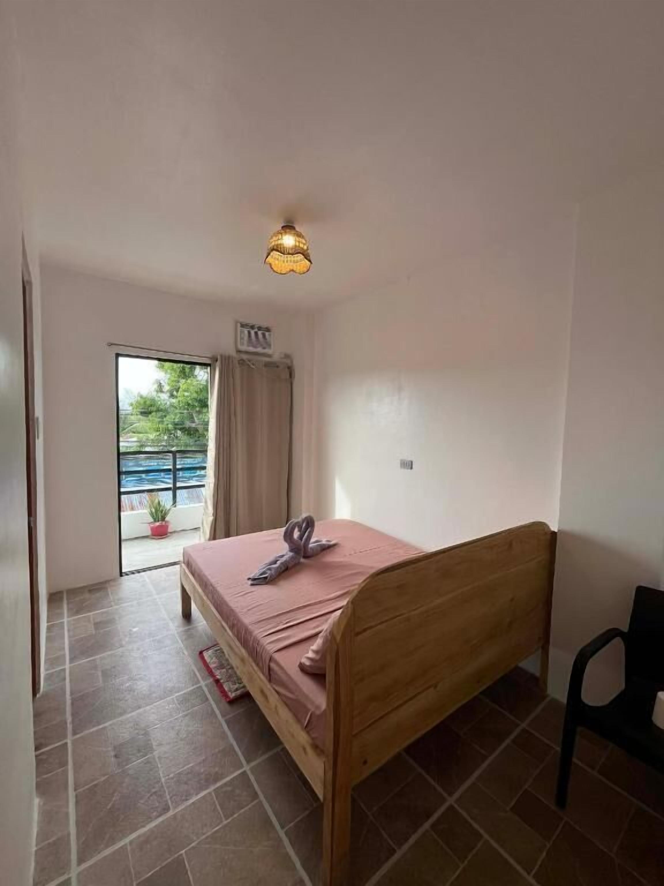 Une chambre avec un lit simple, un luminaire au plafond, une fenêtre avec des rideaux et une vue sur l’extérieur.
