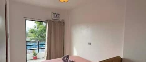 Un dormitorio con una cama individual, una lámpara en el techo, una ventana con cortinas y vistas al exterior.