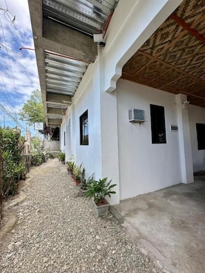 A covered outdoor corridor with a gravel path, potted plants, and a building with a white facade and a wooden ceiling. - Marz inn Moalboal (Moalboal)