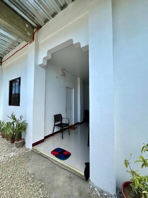 A covered outdoor area with a white wall, a door, a chair, and potted plants. - Marz inn Moalboal (Moalboal)