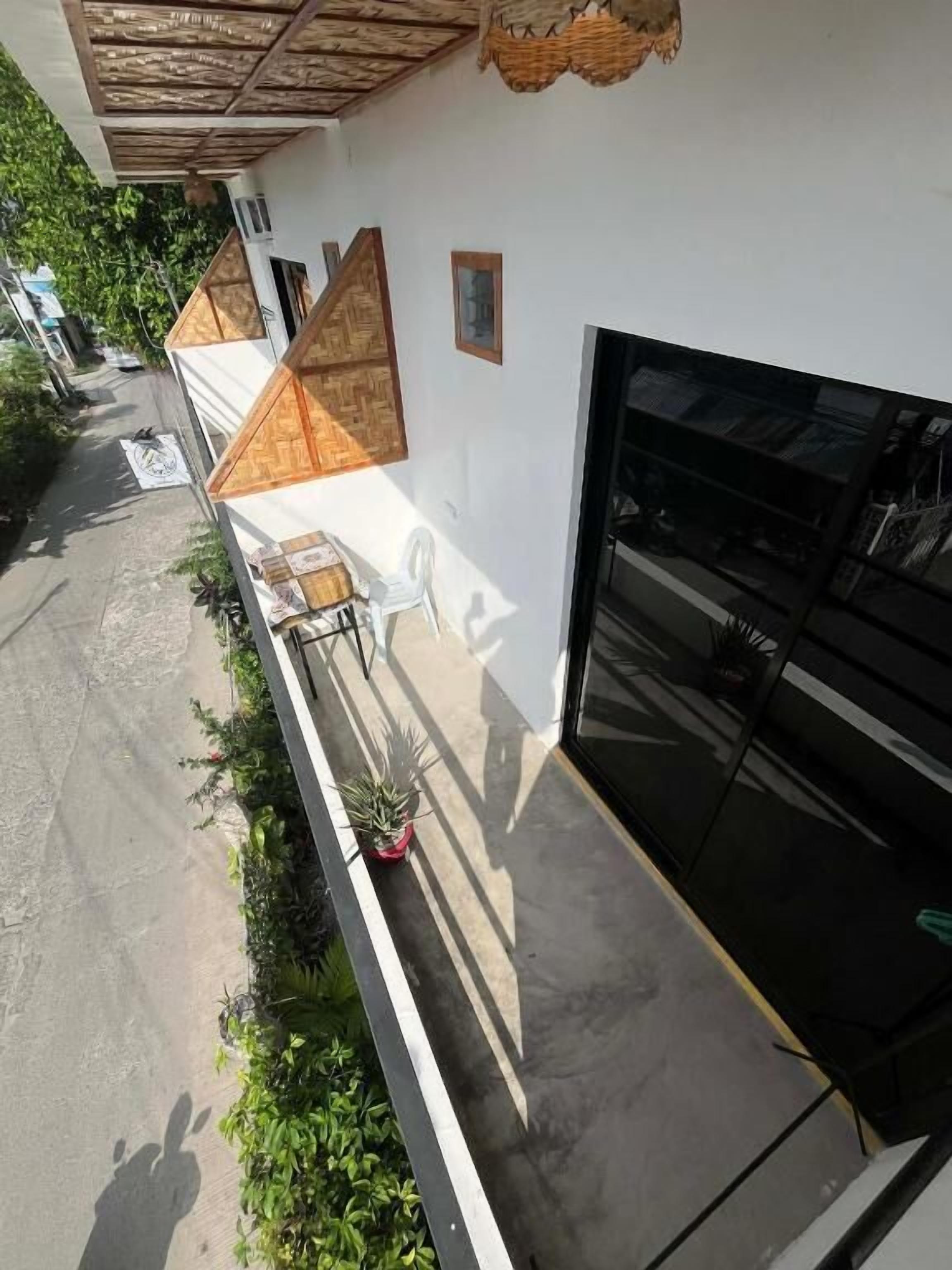 Ein Gebäude mit weißer Fassade, einer schwarzen Garagentür und einem überdachten Außenbereich mit einer Bank und Topfpflanzen.