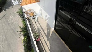 Un edificio con fachada blanca, puerta de garaje negra y un espacio exterior cubierto con un banco y plantas en macetas.