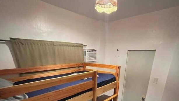Una cama litera con estructura de madera, colchón, una puerta y una lámpara en el techo.