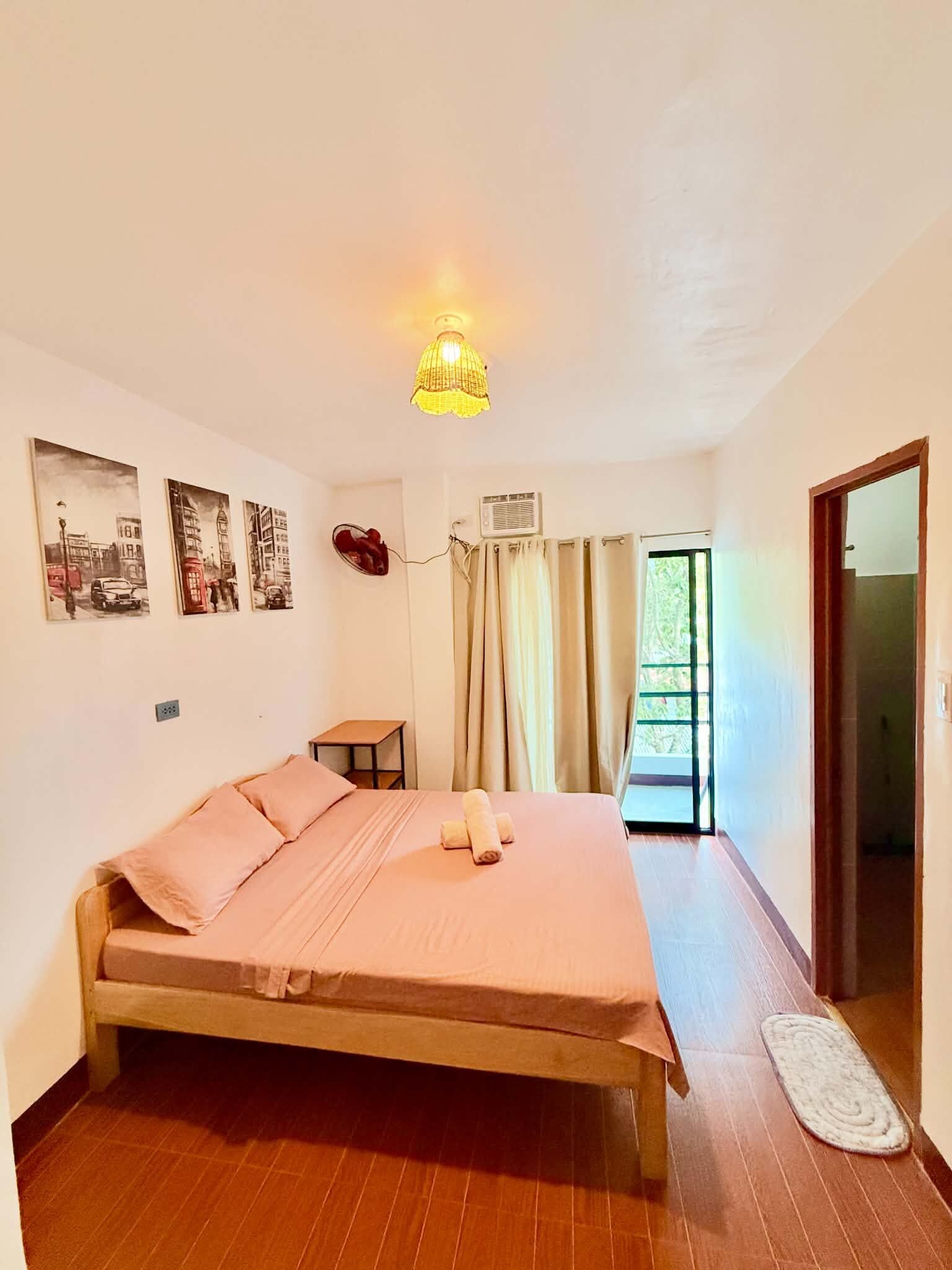 Ein Schlafzimmer mit einem Bett, einem Nachttisch, einer Lampe, einem Fenster mit Vorhängen und Wandbildern.