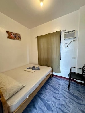 A small room with a single bed, a chair, a window with curtains, and a wall-mounted air conditioning unit. - Marz inn Moalboal (Moalboal)