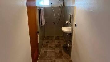 A narrow hallway leading to a bathroom with a shower, a sink, and a ceiling light fixture.
