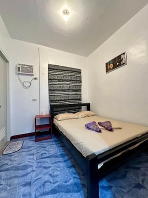 A bedroom with a bed, a small bedside table, a wall-mounted heater, and a patterned rug. - Marz inn Moalboal (Moalboal)