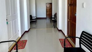 Un pasillo con una puerta a la izquierda, un banco a la derecha y una mesa con sillas al fondo.