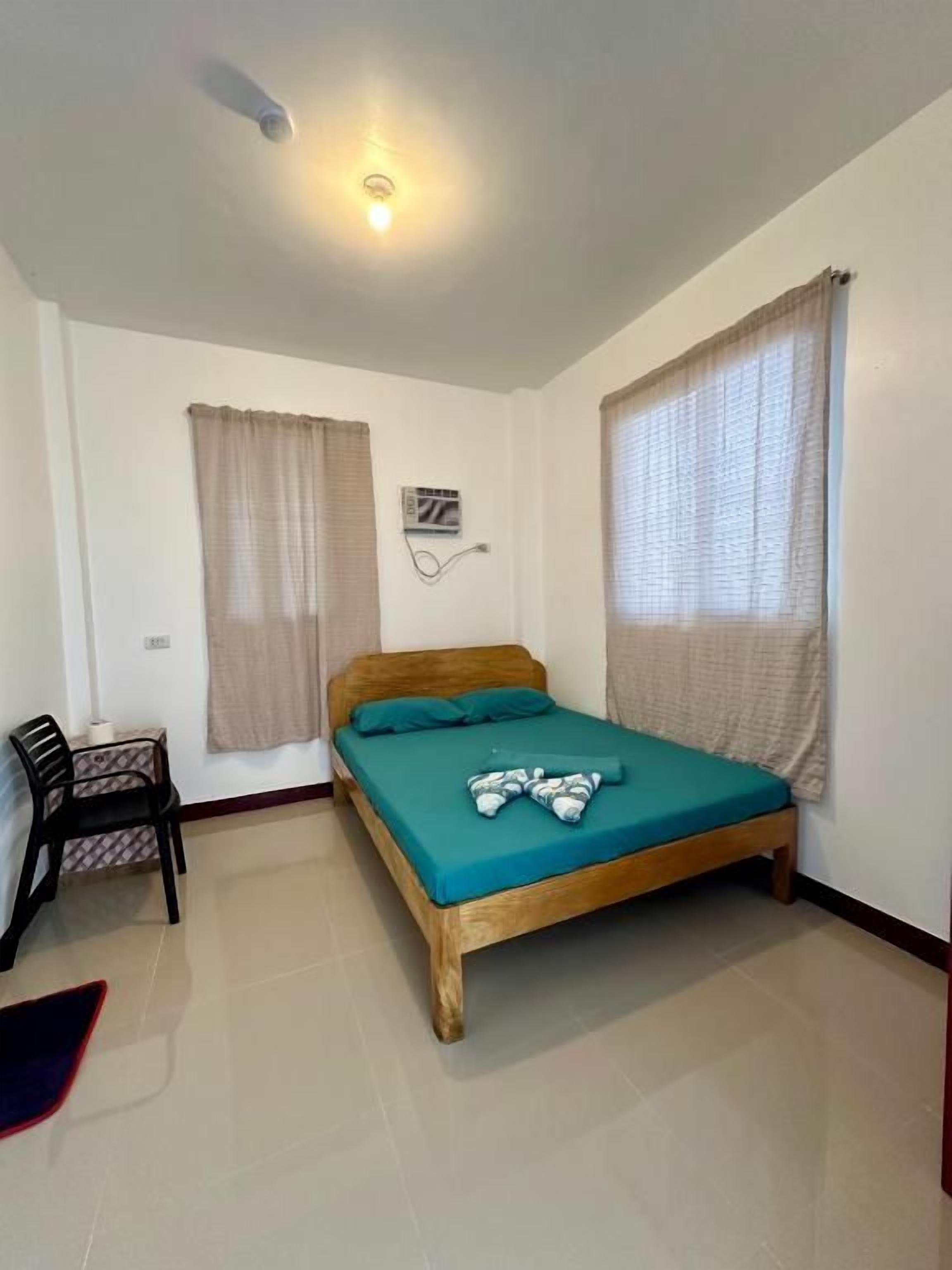 Habitación con una cama individual, estructura de madera, colcha color aguamarina y ventilador de techo.