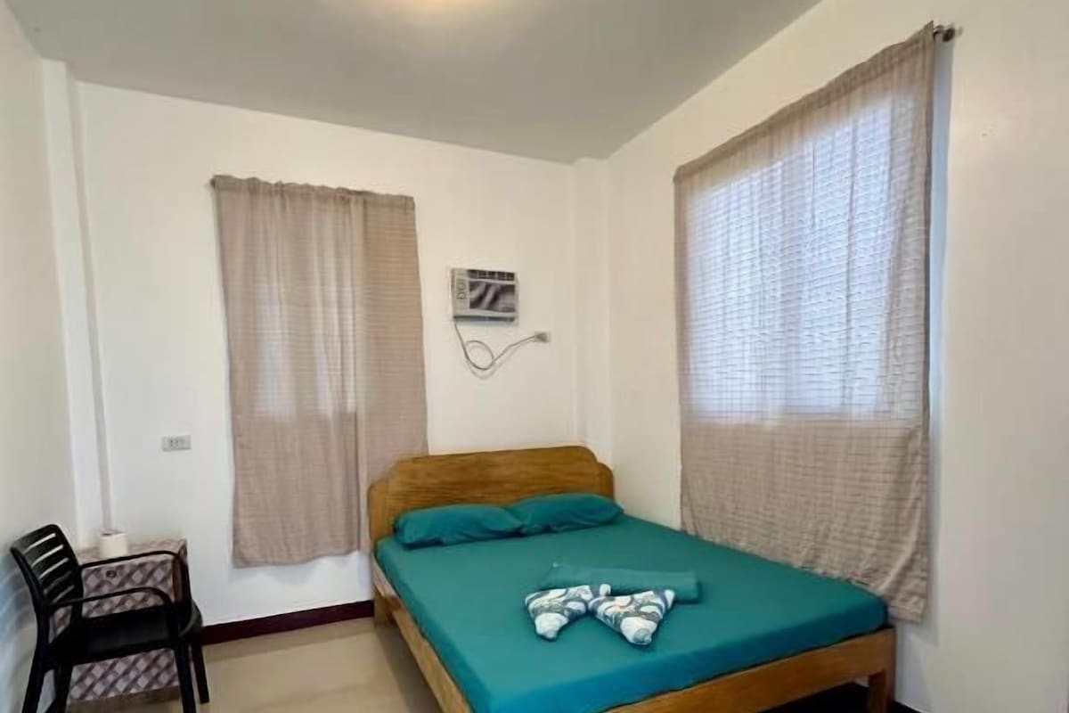 A single-bed room with a wooden frame, a teal bedspread, and a ceiling fan.
