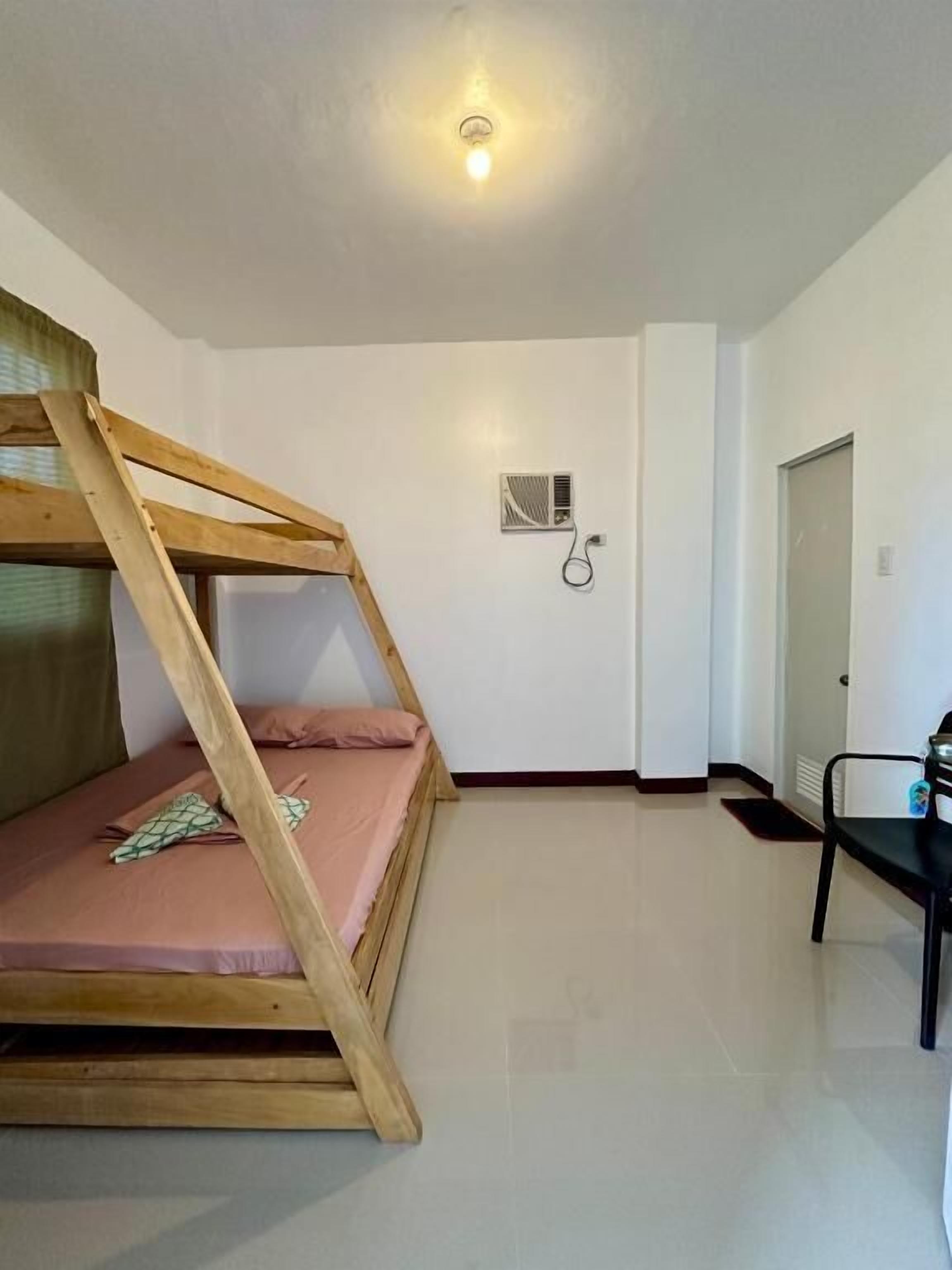 A room with a bunk bed, a chair, a door, and a light fixture on the ceiling.