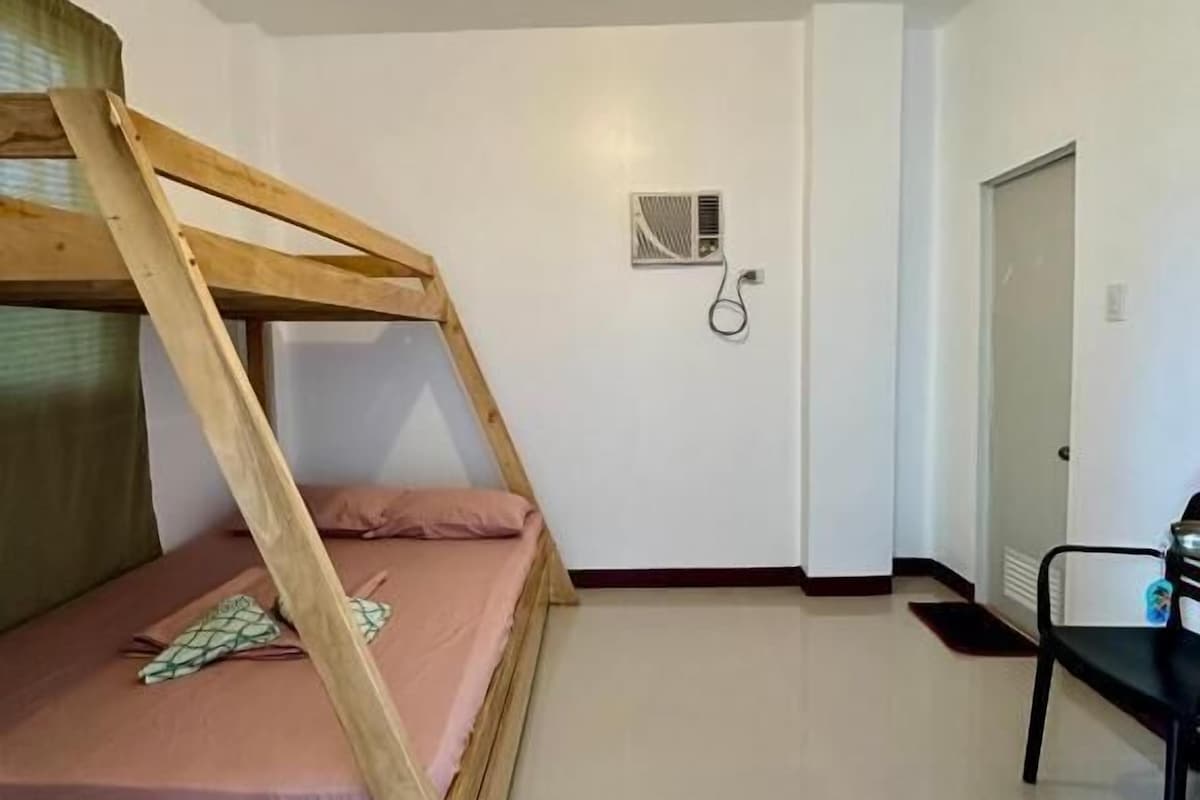 A room with a bunk bed, a chair, a door, and a light fixture on the ceiling.