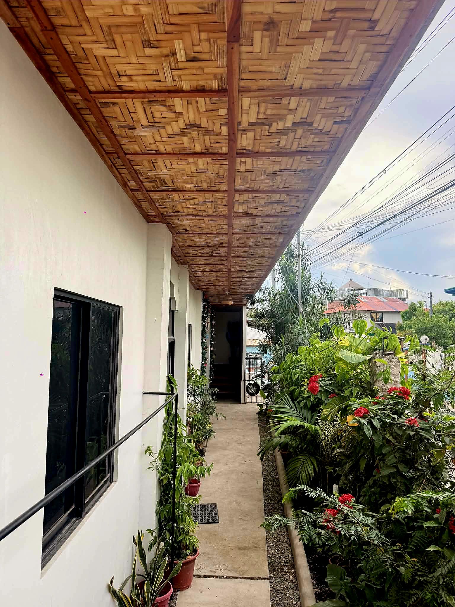 A covered walkway with a wooden ceiling, potted plants, and a view of a residential area.
