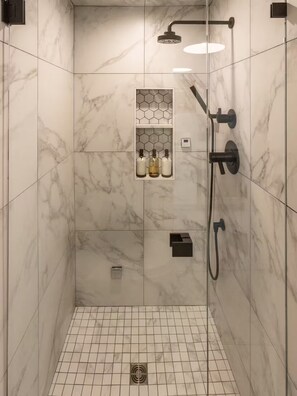 A modern shower with a glass enclosure, a handheld showerhead, a wall-mounted faucet, and a control panel.