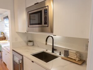 A modern kitchen with a stainless steel microwave, a sink, and a countertop with a potted plant.