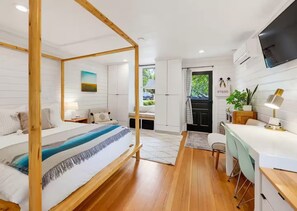 A modern bedroom with a four-poster bed, a desk with a chair, and a television mounted on the wall. - The Studio - Downtown Jacksonville (Jacksonville)