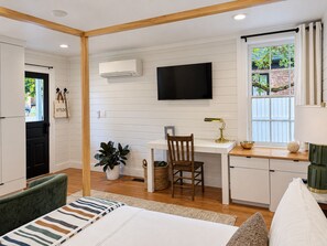 A modern kitchen with a flat-screen TV, wooden beams, a dining area with a chair, and a window with a view of greenery. - The Studio - Downtown Jacksonville (Jacksonville)