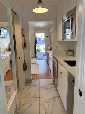 A modern kitchen with white cabinetry, a stainless steel microwave, and a marble floor. - The Studio - Downtown Jacksonville (Jacksonville)