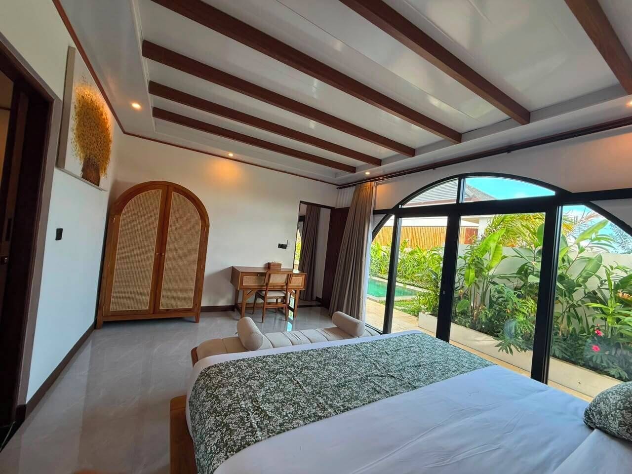 A bedroom with a bed, a desk, and a view of greenery.