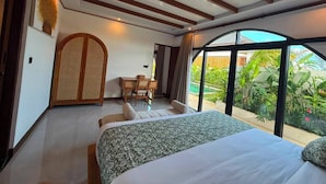 A bedroom with a bed, a desk, and a view of greenery. - Casa Anagata Pandawa (Badung)