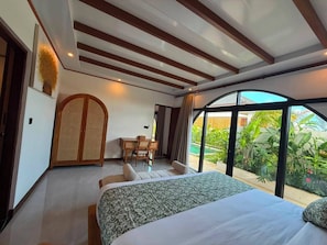 A bedroom with a bed, a desk, and a view of greenery. - Casa Anagata Pandawa (Badung)