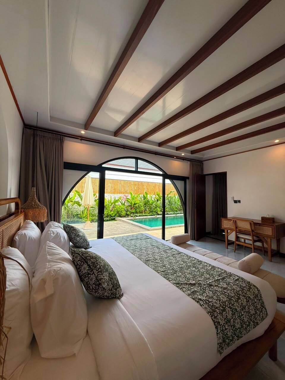 Un dormitorio con una cama grande, un escritorio y vista a una piscina.