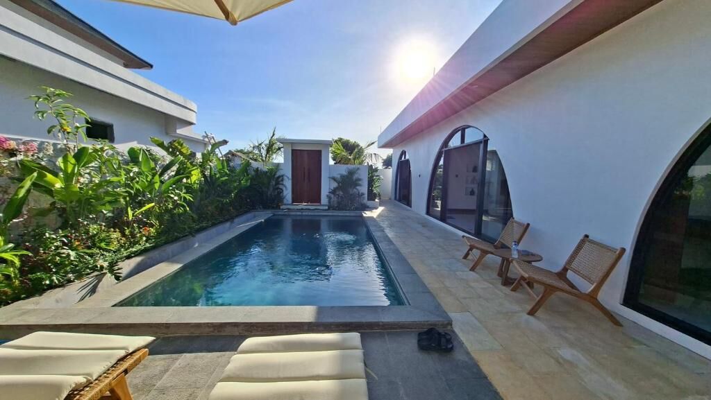 Una piscina con sillones de descanso y una zona de estar cubierta, rodeada de exuberante vegetación y arquitectura moderna.