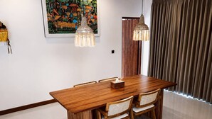 A dining area with a wooden table, wicker chairs, and pendant lights. - Casa Anagata Pandawa (Badung)