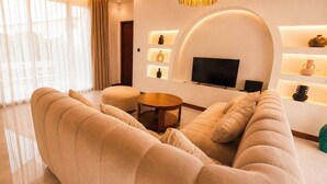 A modern living room with a large beige sofa, a round coffee table, and a flat-screen TV mounted on a white wall. - Casa Anagata Pandawa (Badung)