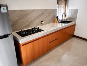 A kitchen with a built-in gas stove, a sink, wooden cabinets, and a marble backsplash. - Casa Anagata Pandawa (Badung)