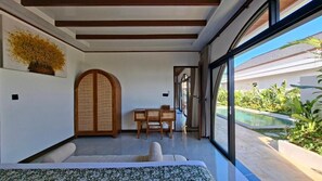 A modern interior with a bed, a dining area, and a view of a swimming pool. - Casa Anagata Pandawa (Badung)