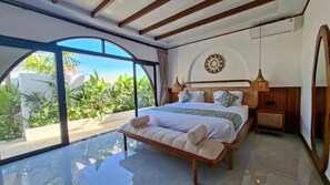 A bedroom with a large bed, a bedside table, a mirror, and a view of greenery outside. - Casa Anagata Pandawa (Badung)