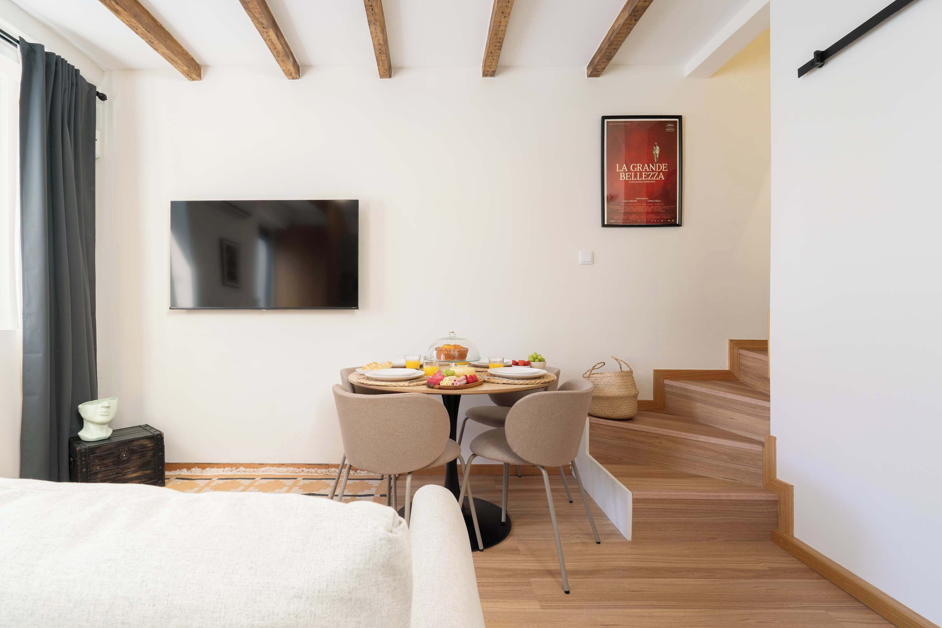 Una habitación moderna con cama, una mesa de comedor con desayuno, televisor y una escalera.