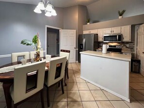 A modern kitchen with white cabinetry, a central island, and a dining area with a table and chairs.