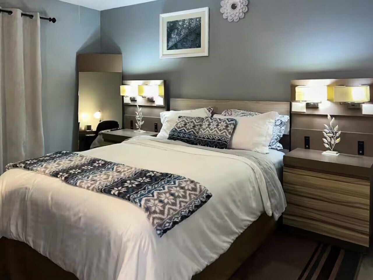 Una habitación de hotel con una cama grande, lámparas de noche, un espejo y una obra de arte colgada en la pared.