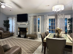 Una sala de estar con chimenea, televisor y comedor con sillas y mesa.