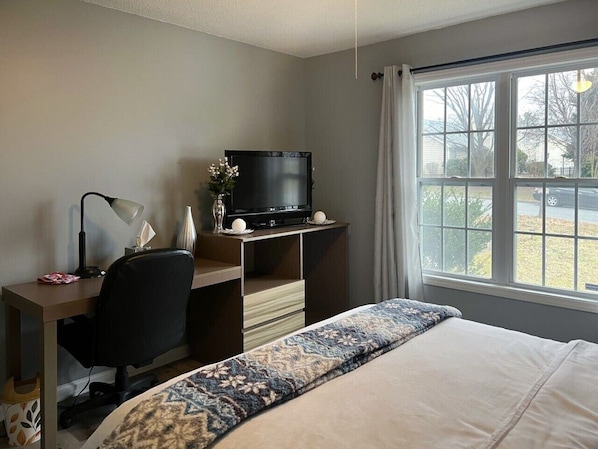 A hotel room with a bed, a desk with a computer, a television, and a window with a view of the outdoors.