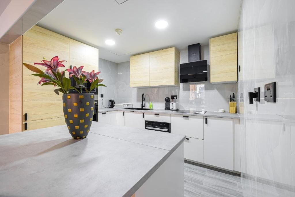 Una cocina moderna con armarios blancos, encimera de mármol y un florero con flores.
