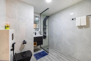 Un baño moderno con cabina de ducha de vidrio, inodoro negro y alfombra azul.