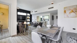 Un espace de vie moderne comprenant un coin repas, un ensemble de canapés, un téléviseur à écran plat et une cuisine en arrière-plan.