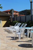 Mobiliário de exterior com cadeiras e mesas de plástico branco, dispostas num terraço de pedra.