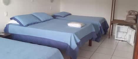 A hotel room with two beds, a small table, a mirror, and a shelf with bags.