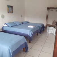 Quarto de hotel com duas camas, uma mesinha, um espelho e uma estante com malas.
