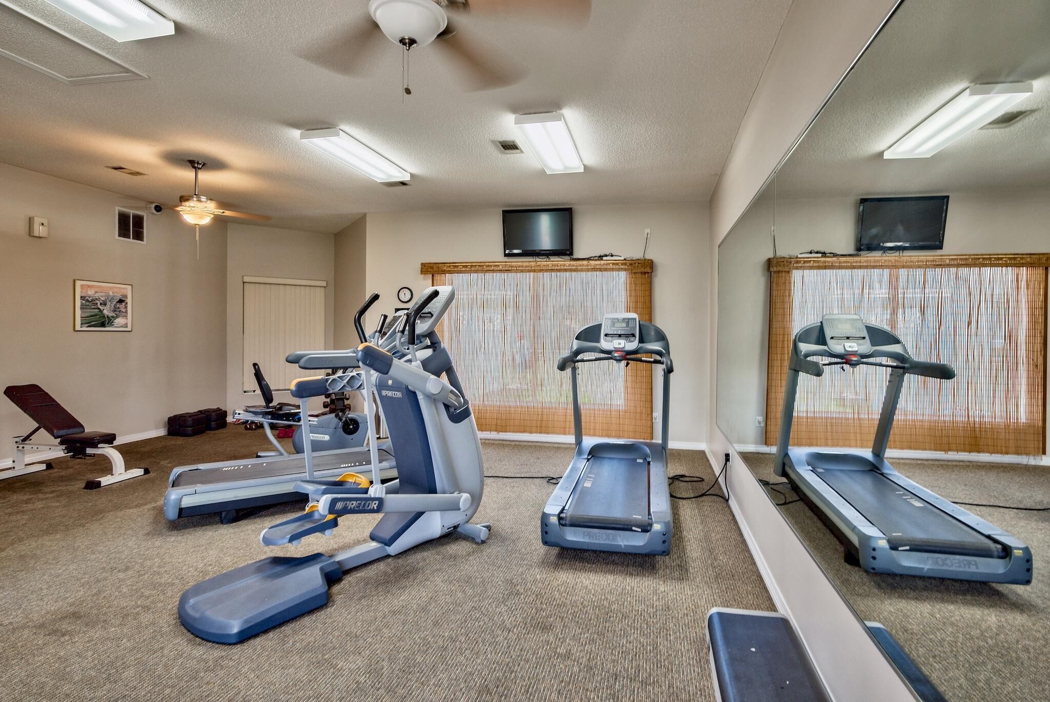 A gym with treadmills, elliptical machines, and a bench.