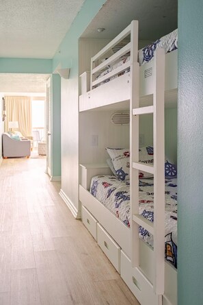 A bunk bed with drawers, a bedside table, and a window with curtains. - Pelican Beach Resort 904- Seaside Serenity (Destin)