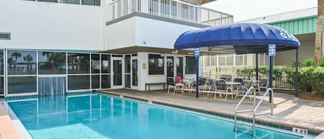 Une piscine dotée d’un espace de repos couvert et d’un bâtiment à deux étages avec des balcons.
