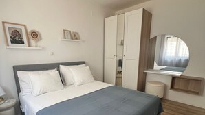 Quarto com cama, guarda-roupa, televisão e uma pequena mesa.